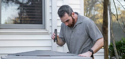 HVAC technician inspecting an outdoor AC condenser unit beside a home