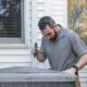 HVAC technician inspecting an outdoor AC condenser unit beside a home